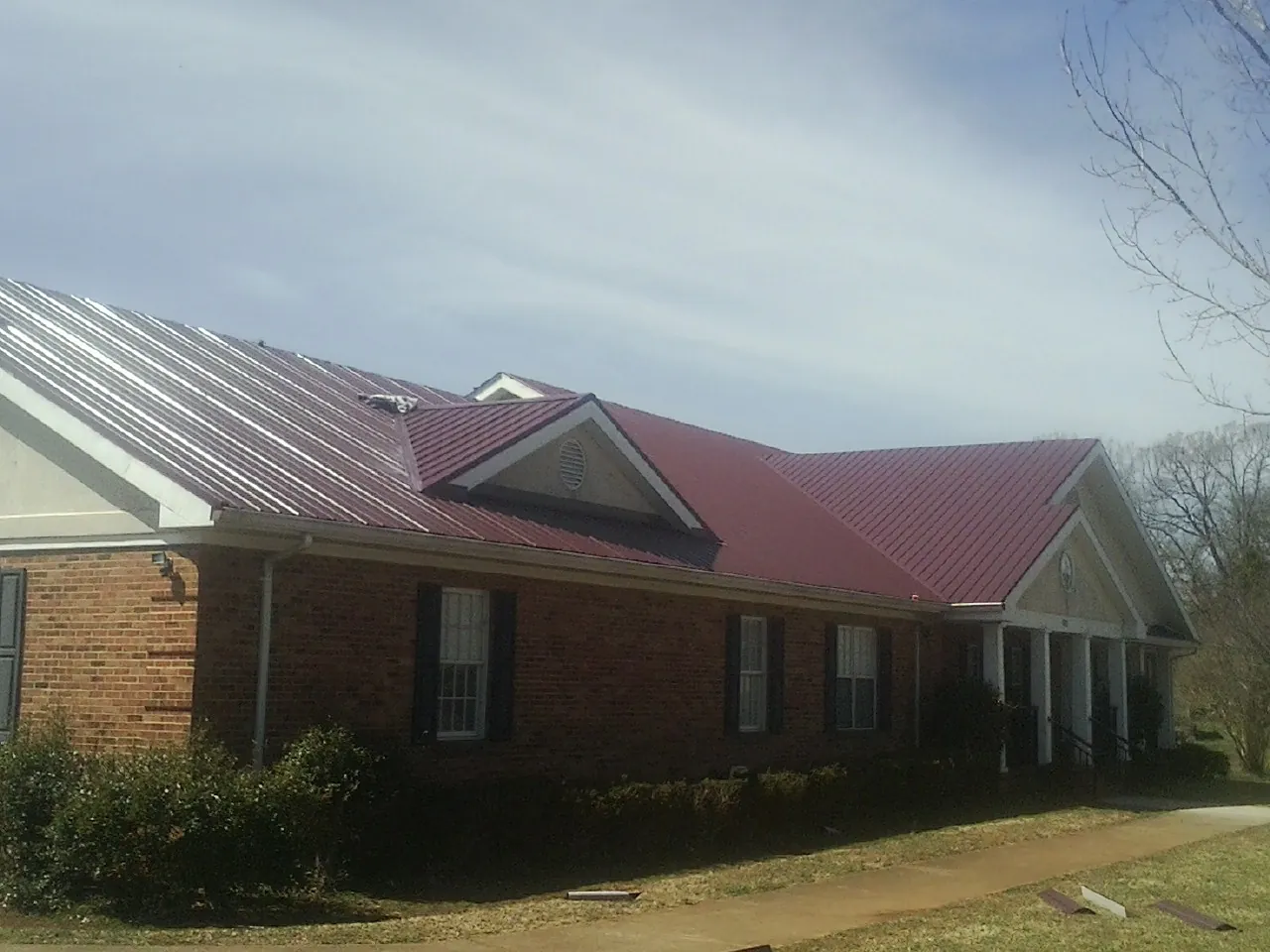 Red metal roof with gabled entries on a long brick building, from a Hail Damage Roof Repair job in Reidsville