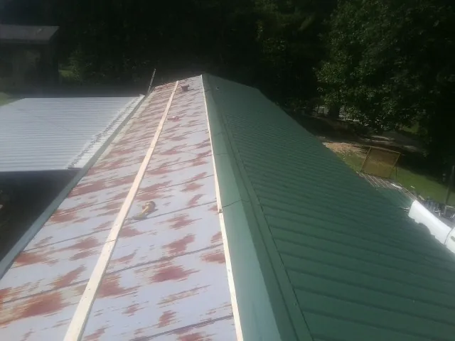 Old rusted panels beside newly installed green metal roofing — Wind Damage Roof Repair by Roofing Brothers in Reidsville