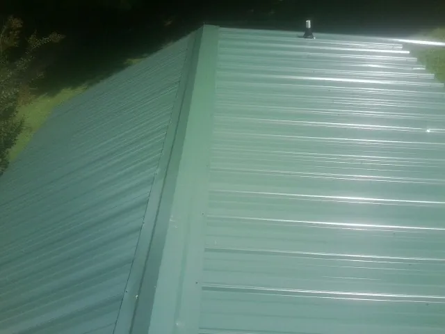 New green metal panels meeting at the ridge of a roof — Flat Roof Repair work by our crew in Reidsville
