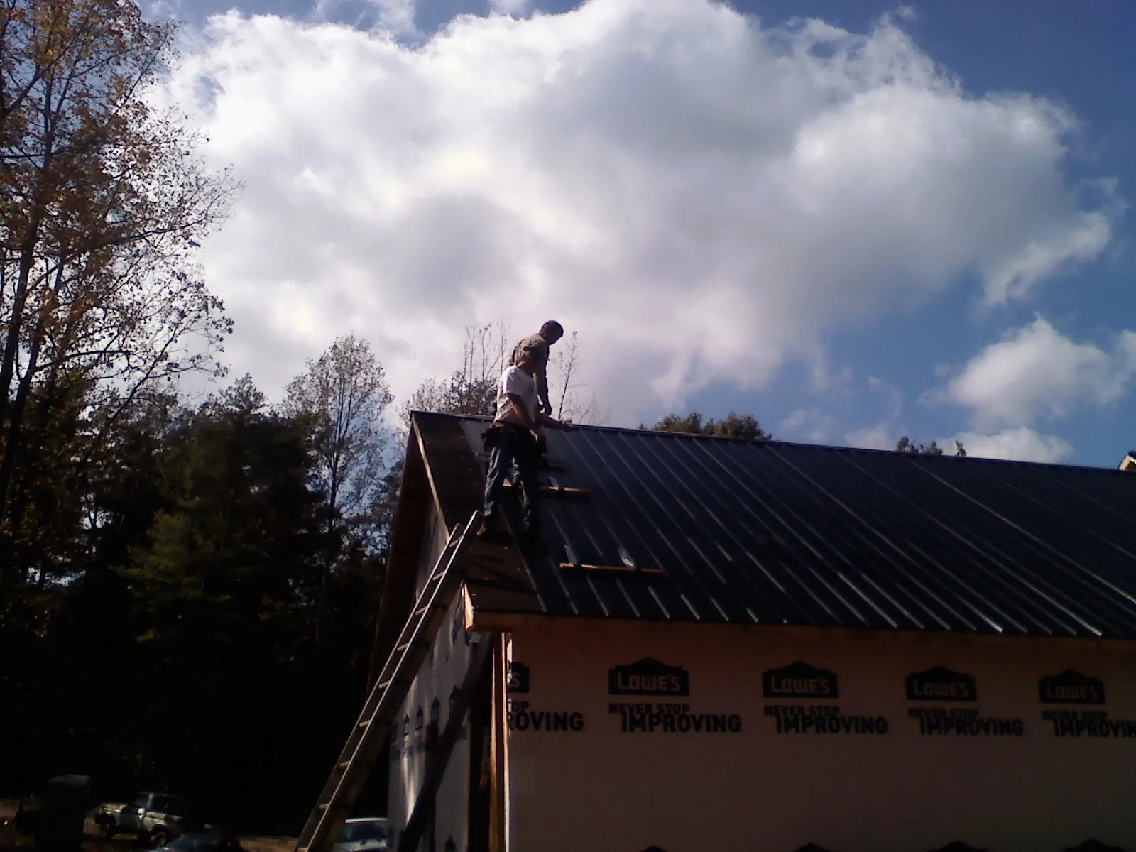 Roofer fastening dark metal panels high against a cloudy sky, from a Roof Inspection job in Reidsville