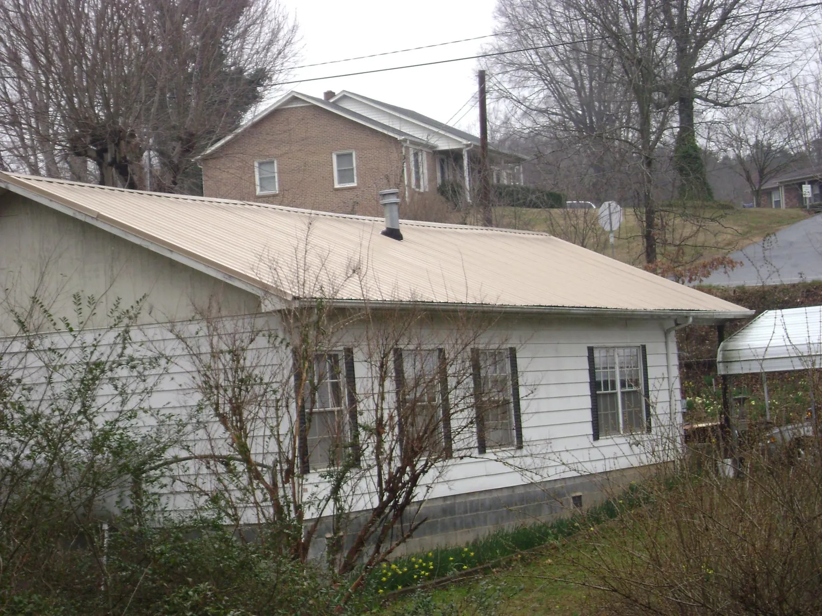 Tan metal roof on a white sided house set into a hillside — Commercial Roofing by Roofing Brothers in Reidsville