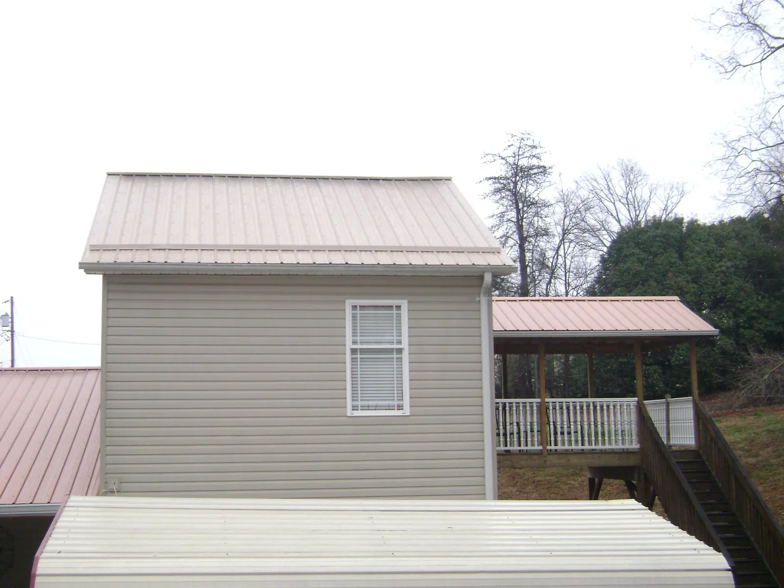 Tan metal roofs on a two story addition and attached porch, from a Roof Replacement job in Reidsville